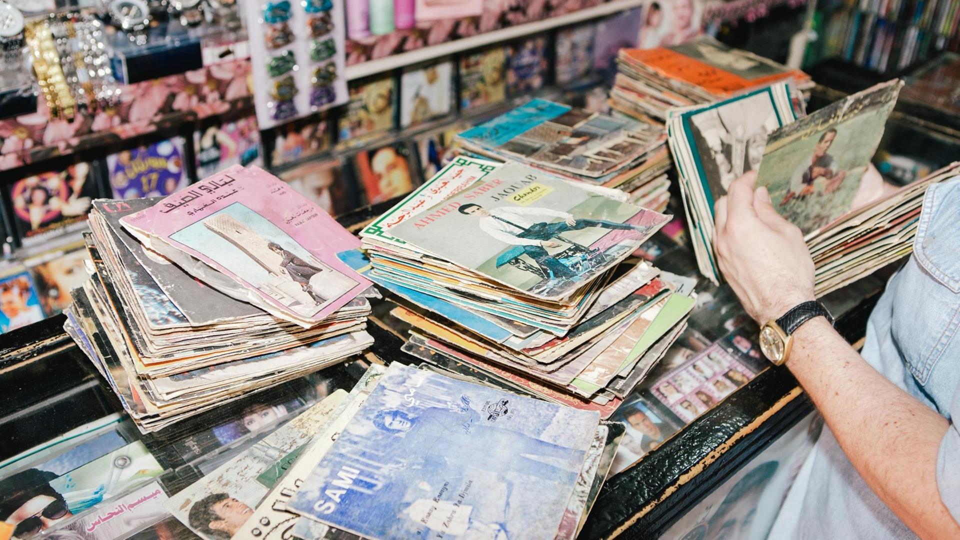 Ein Mann steht vor mehreren bunten Stapeln mit Vinyl-Singles und blättert darin Ein Mann steht vor mehreren bunten Stapeln mit Vinyl-Singles und blättert darin