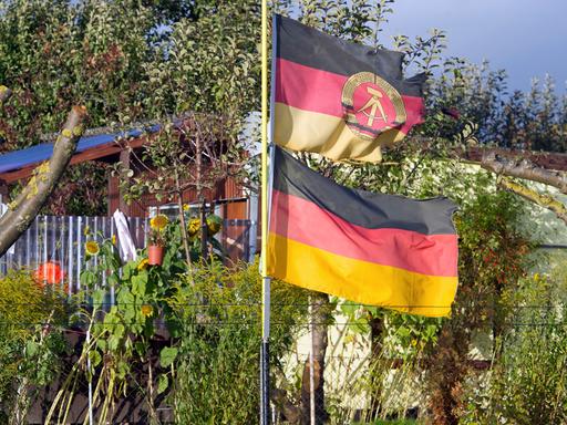 Eine DDR-Fahne und eine Deutschland-Flagge wehen an einem Fahnenmast in der Kleingartenanlage "Samtenser Frühling" in Samtens auf der Ostseeinsel Rügen.