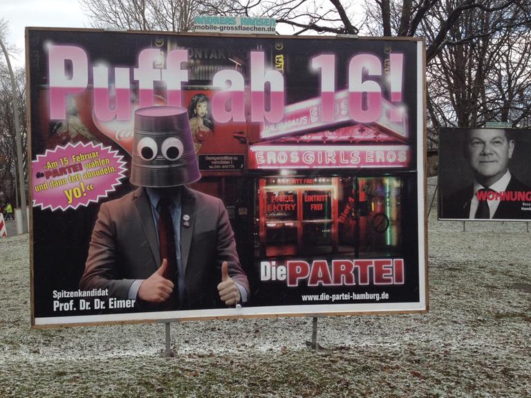 Großes Wahlplakat auf einer Grünfläche mit der Forderung: "Puff ab 16" und einem Bild von einem Mann, der einen Eimer auf dem Kopf trägt, im Hintergrund ist ein Bordell zu sehen.