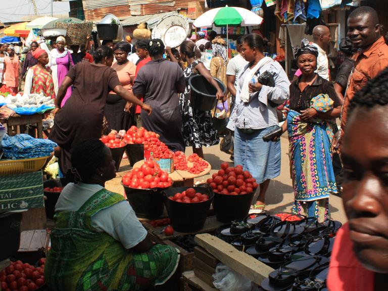Menschen auf Markt in Afrika stehen vor Stand.