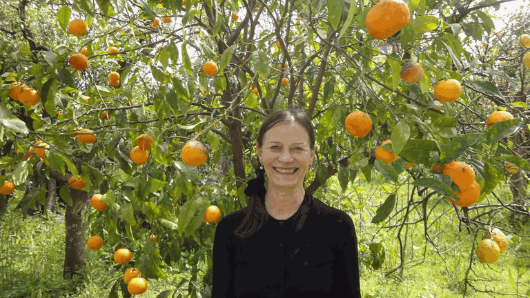 Die Tänzerin Sighilt Pahl steht vor einem Orangenbaum und lächelt in die Kamera. Die Tänzerin Sighilt Pahl steht vor einem Orangenbaum und lächelt in die Kamera.