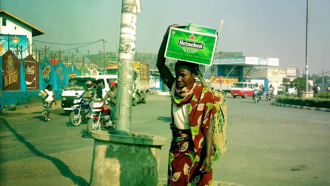 Eine Frau steht auf einer Verkehrsinsel in Goma im Kongo und trägt eine Kiste mit Heineken-Bier auf dem Kopf, aufgenommen 2013 Eine Frau steht auf einer Verkehrsinsel in Goma im Kongo und trägt eine Kiste mit Heineken-Bier auf dem Kopf, aufgenommen 2013