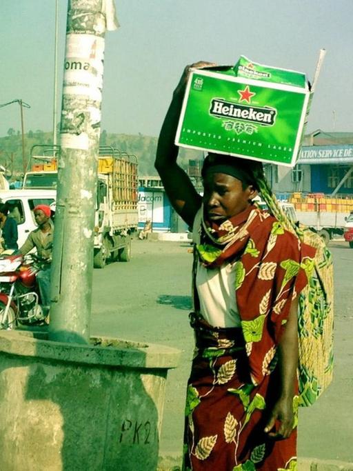 Eine Frau steht auf einer Verkehrsinsel in Goma im Kongo und trägt eine Kiste mit Heineken-Bier auf dem Kopf, aufgenommen 2013