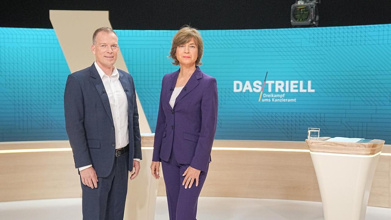 Die Moderatoren Oliver Köhr und Maybrit Illner stehen im Fernsehstudio. Die Moderatoren Oliver Köhr und Maybrit Illner stehen im Fernsehstudio.