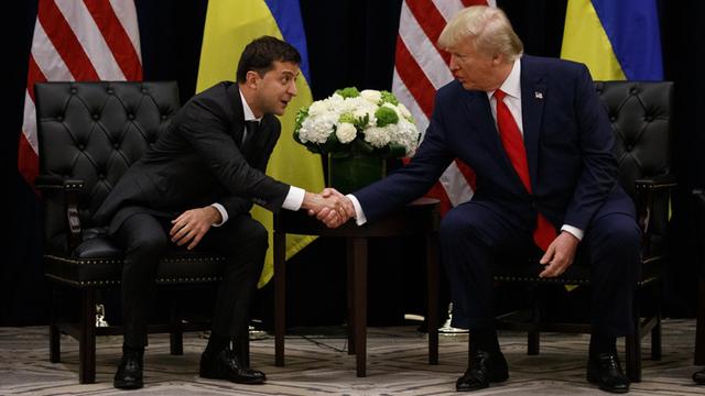 Donald Trump und Wolodymyr Selenskyj sitzen vor ihren Landesflaggen und geben sich die Hand.