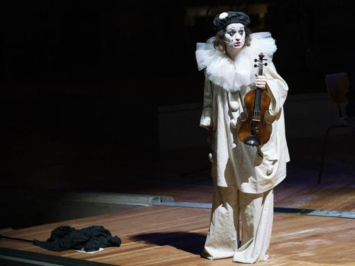 Die Geigerin in einem weißen Pirrot-Kostüm, ihr Instrument in der Hand.