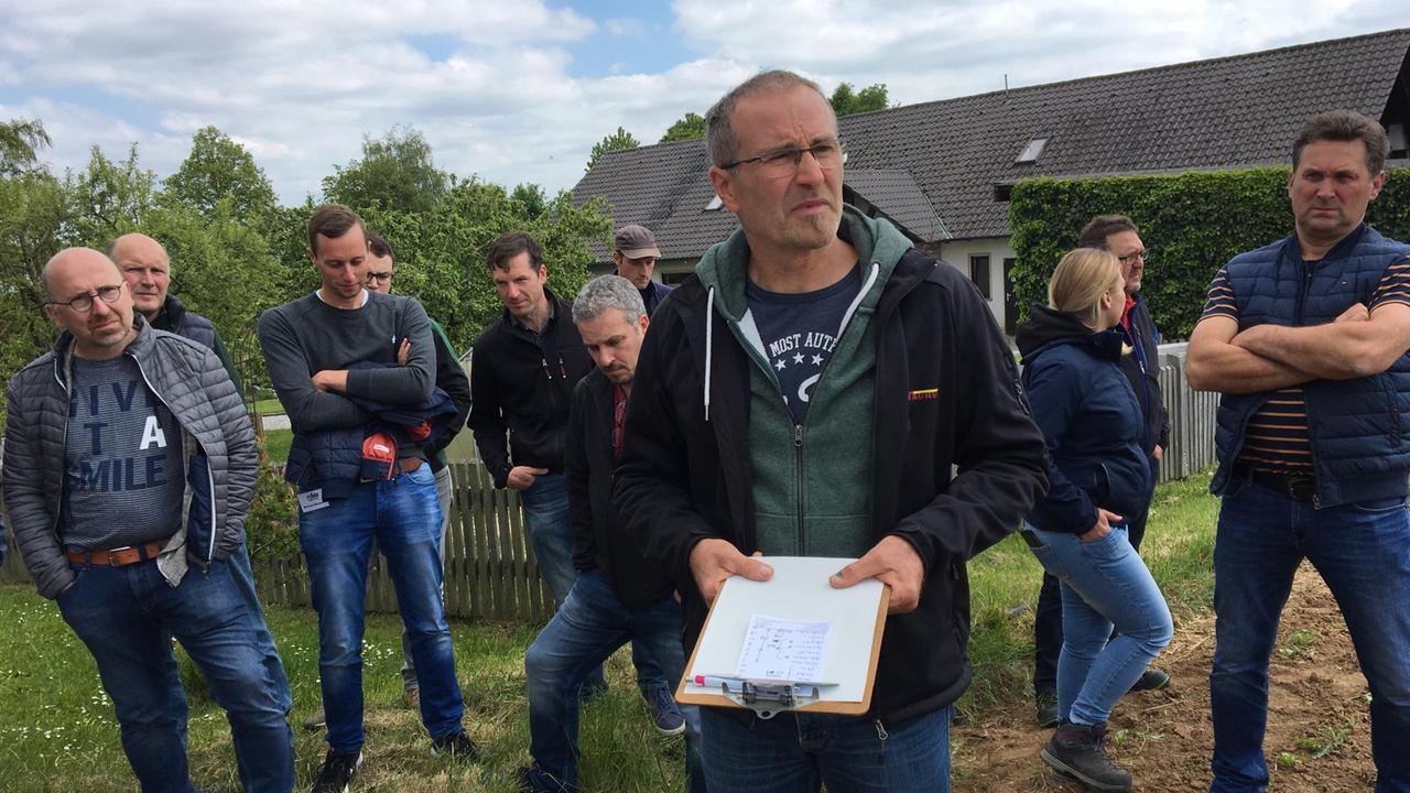 Andreas Römert steht auf seinem Hof, um ihn herum mehrere Landwirte, die ihm zuhören.