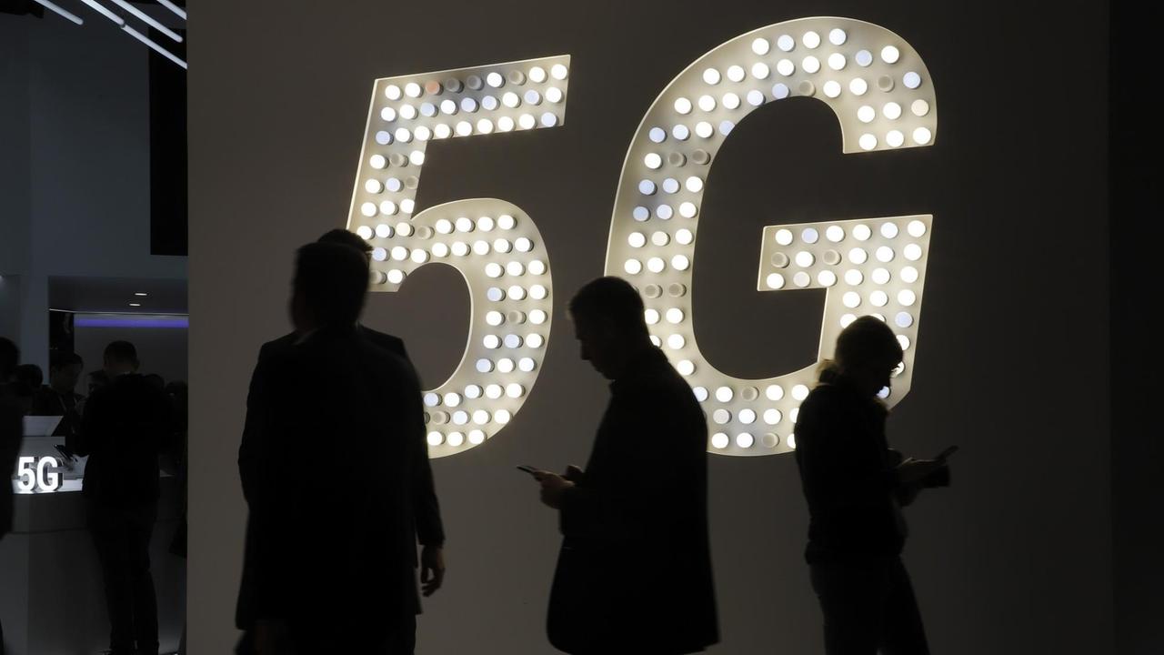 Besucher der Technikmesse Mobile World Congress Gehen an einer Leuchttafel für den Funkstandard 5G vorbei.