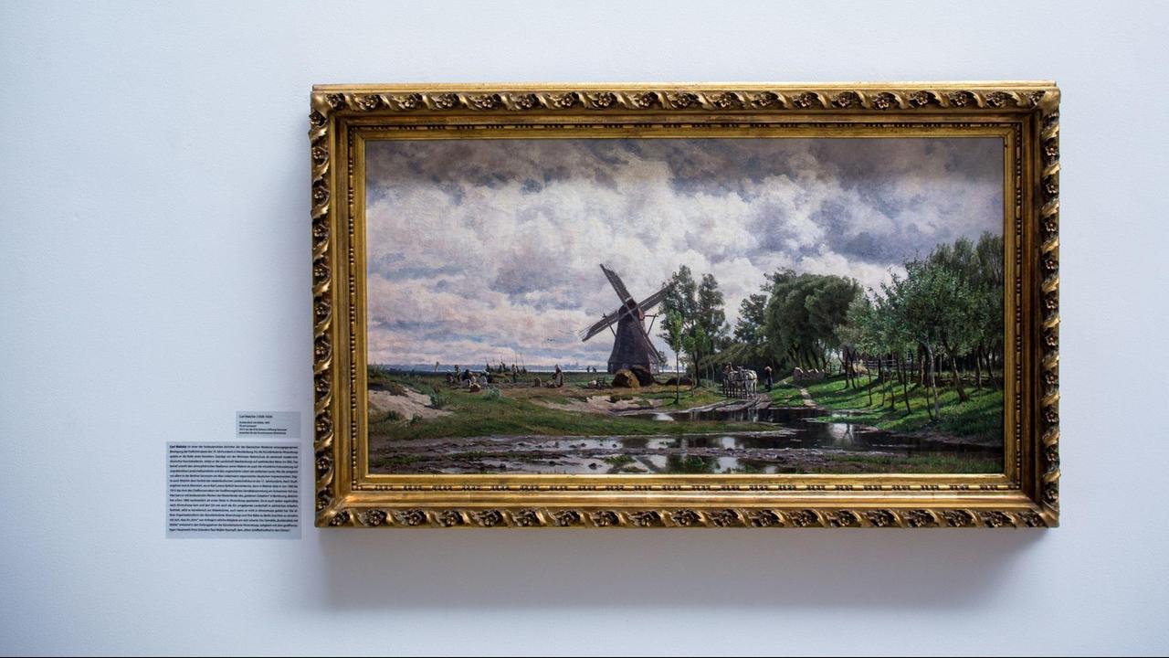 Das Gemälde "Boddenblick mit Mühle" hängt an einer weißen Wand. Das Gemälde "Boddenblick mit Mühle" hängt an einer weißen Wand.