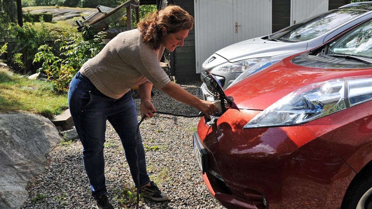 Eine Frau steckt ein Kabel in ihren Elektro-Nissan, um das Auto zu laden. Eine Frau steckt ein Kabel in ihren Elektro-Nissan, um das Auto zu laden.