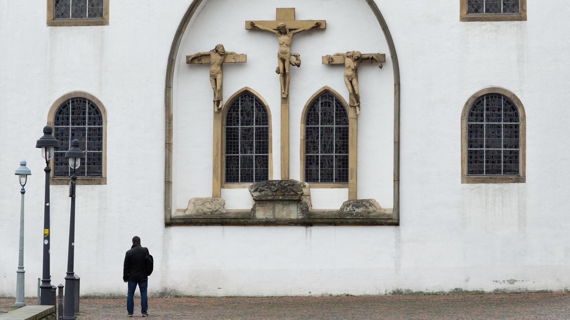 19.12.2018, Niedersachsen, Osnabrück: Ein Mann steht vor der Kleinen Kirche am Osnabrücker Dom und blickt auf eine Fassade mit Kreuzen.