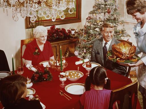 Eine Aufnahe von 1965 zeigt eine Frau, die einen großen Truthahn zum Weihnachtsessen auf den Tisch bringt. Dort sitzen Großeltern und Kinder am gedeckten Tisch. Im Hintergrund ist ein geschmückter Weihnachtsbaum zu sehen.