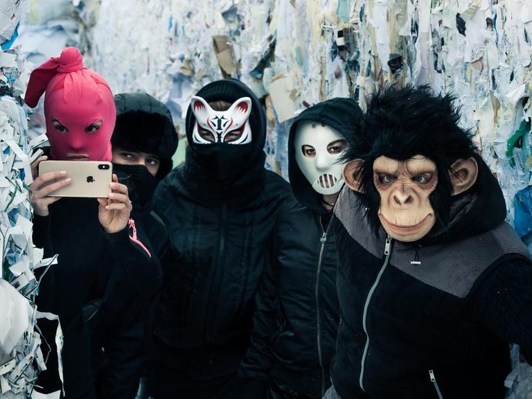 Fünf Jugendliche in dunklen Klamotten und mit Masken vor den Gesichtern.