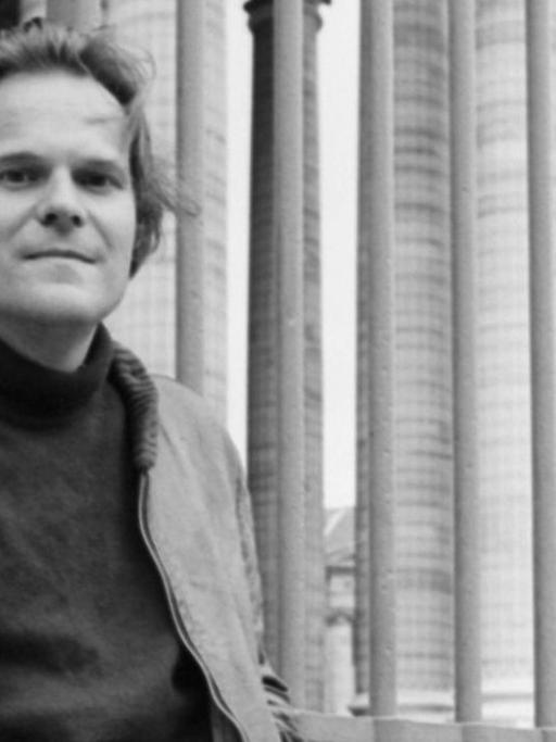 Schwarzweißfoto: Der Schriftsteller Peter Schneider lehnt lässig an einem Zaun.