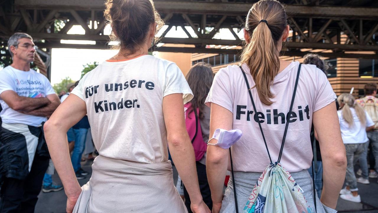 Aufnahme zweier Frauen von hinten. Beide tragen bedruckte T-Shirt mit der Aufschrift 'für unsere Kinder.' und 'Freiheit'.