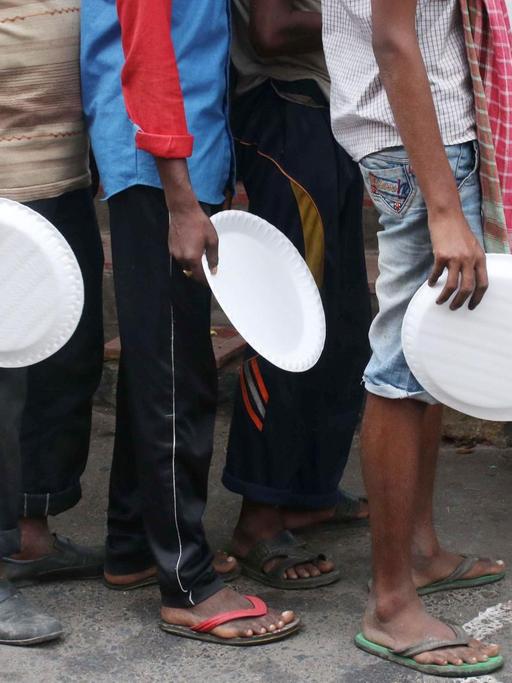 Menschen in ärmlicher Kleidung mit Tellern in der Hand warten auf eine Essensausgabe in Kalkutta (Indien), inmitten der Covid-19 Pandemie, 27. August 2020.