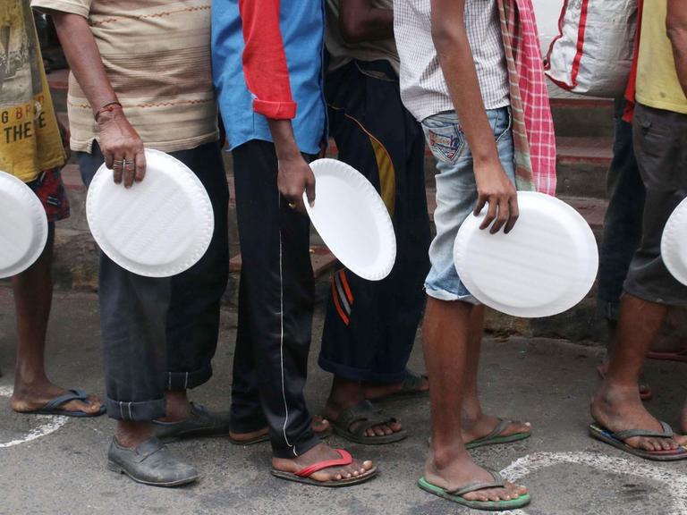 Menschen in ärmlicher Kleidung mit Tellern in der Hand warten auf eine Essensausgabe in Kalkutta (Indien), inmitten der Covid-19 Pandemie, 27. August 2020.