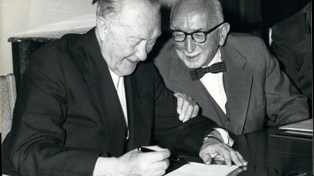 Bundeskanzler Konrad Adenauer sitz zu einer Unterschrift an einem Tisch neben Justizminister Fritz Schaffer. Dieser fasst Adenauer am Unterarm, beide lachen. Bundeskanzler Konrad Adenauer sitz zu einer Unterschrift an einem Tisch neben Justizminister Fritz Schaffer. Dieser fasst Adenauer am Unterarm, beide lachen.