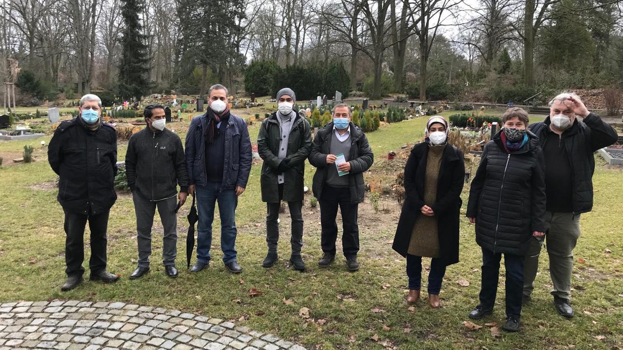 Acht erwachsene Männer und Frauen haben sich für ein Foto auf dem Gräberfeld nebeneinander aufgestellt. Acht erwachsene Männer und Frauen haben sich für ein Foto auf dem Gräberfeld nebeneinander aufgestellt.
