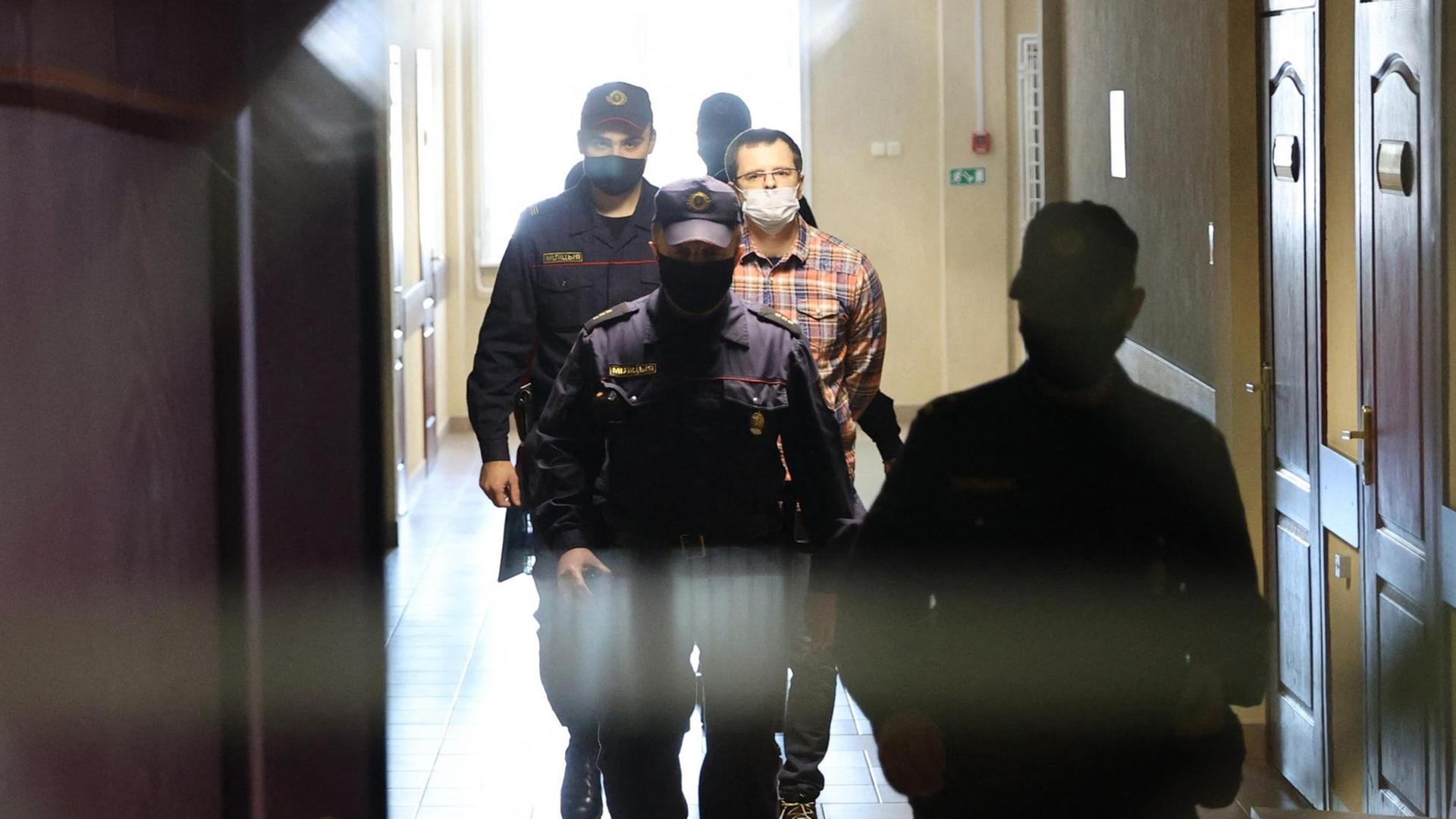 Ein Mann wird durch einen Flur von mehreren Polizisten vor Gericht geführt. Ein Mann wird durch einen Flur von mehreren Polizisten vor Gericht geführt.