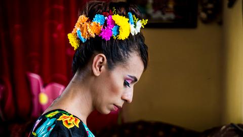 Naomy Mendez, mit einem Kranz um die dunkelhaarige Hochsteckfrisur, sitzt im Profil zur Kamera und blickt nach unten.