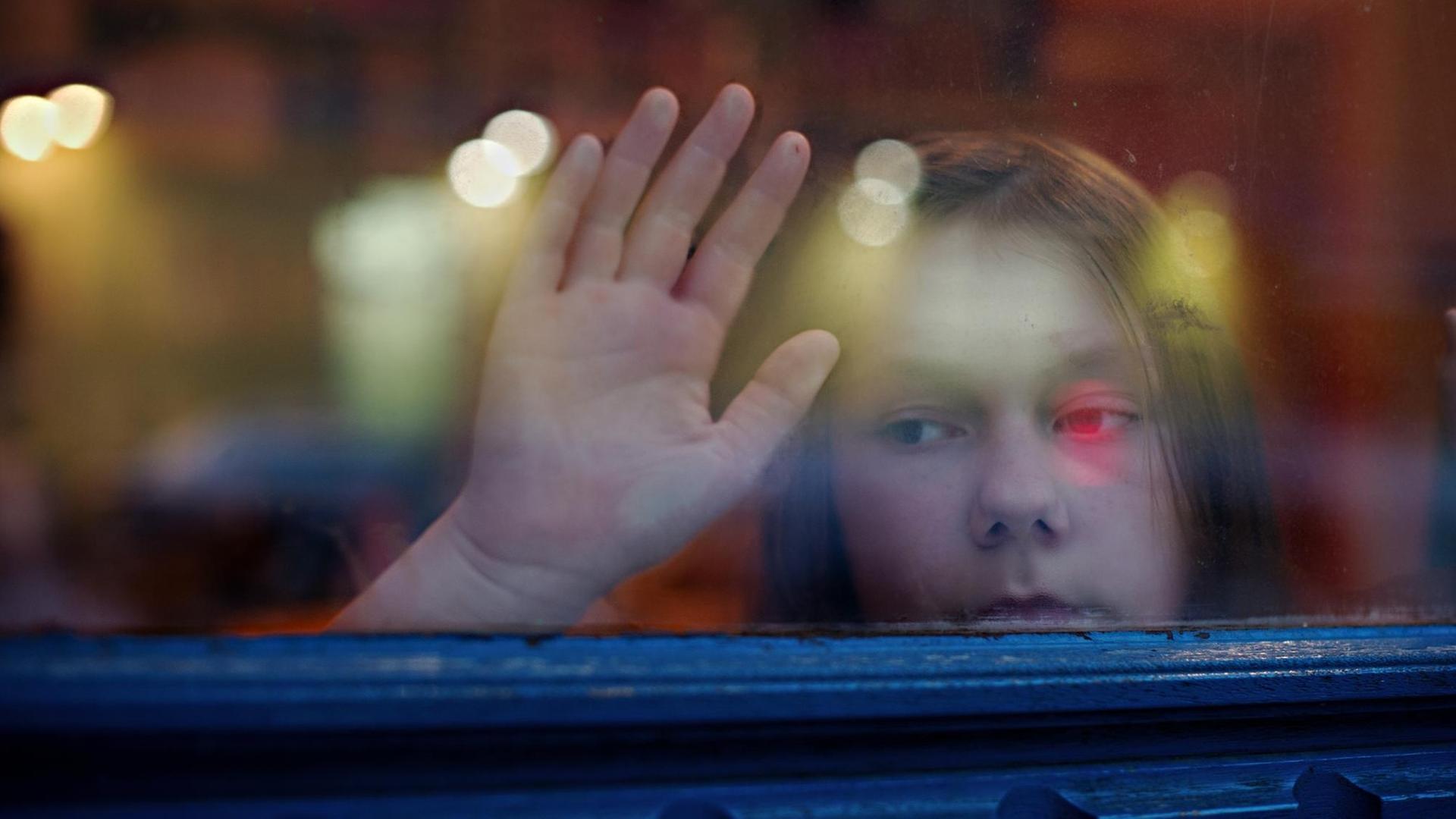 Ein junges Mädchen blickt in Berlin aus einem Fenster