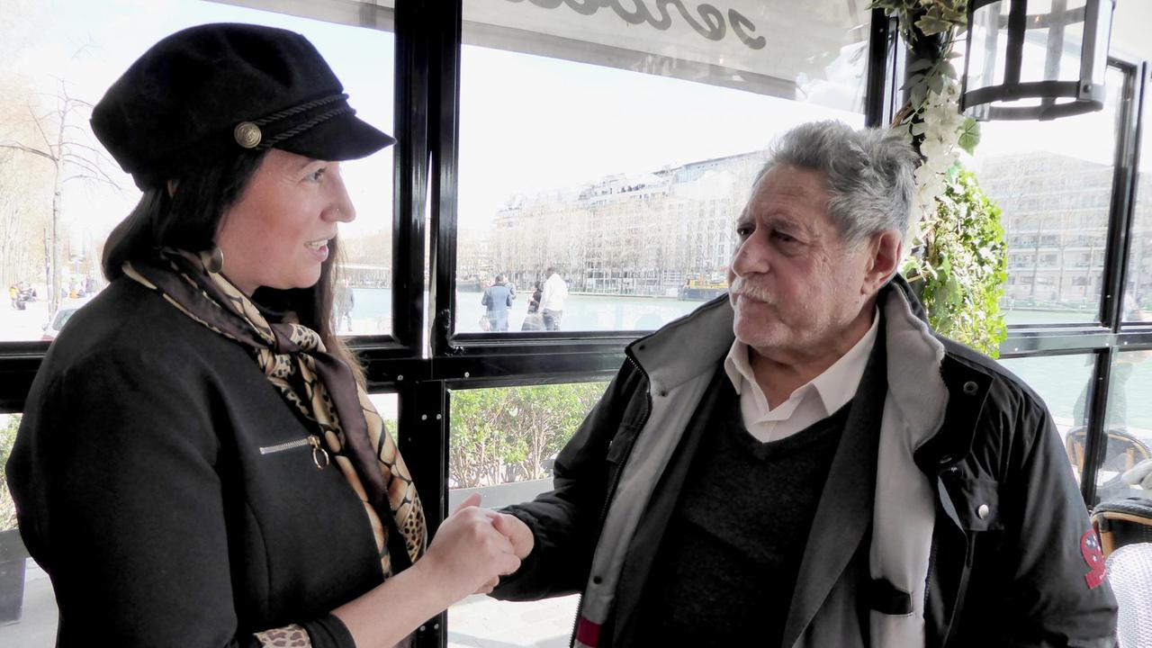 Eine Frau mit dunklen Haaren reicht einem älteren Mann mit grauen Haaren und Schnauzbart die Hand Eine Frau mit dunklen Haaren reicht einem älteren Mann mit grauen Haaren und Schnauzbart die Hand