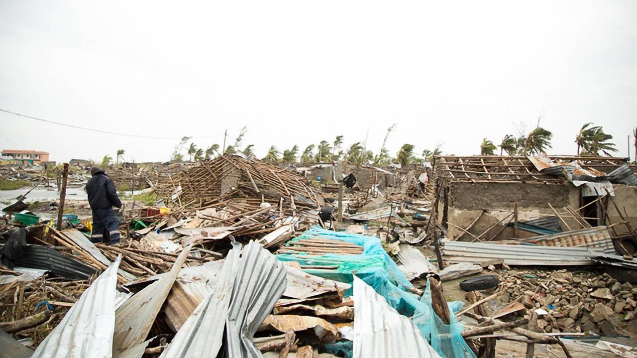 Zerstörte Hütten und Häuser, dazwischen ein Mann auf der Suche nach Überresten.