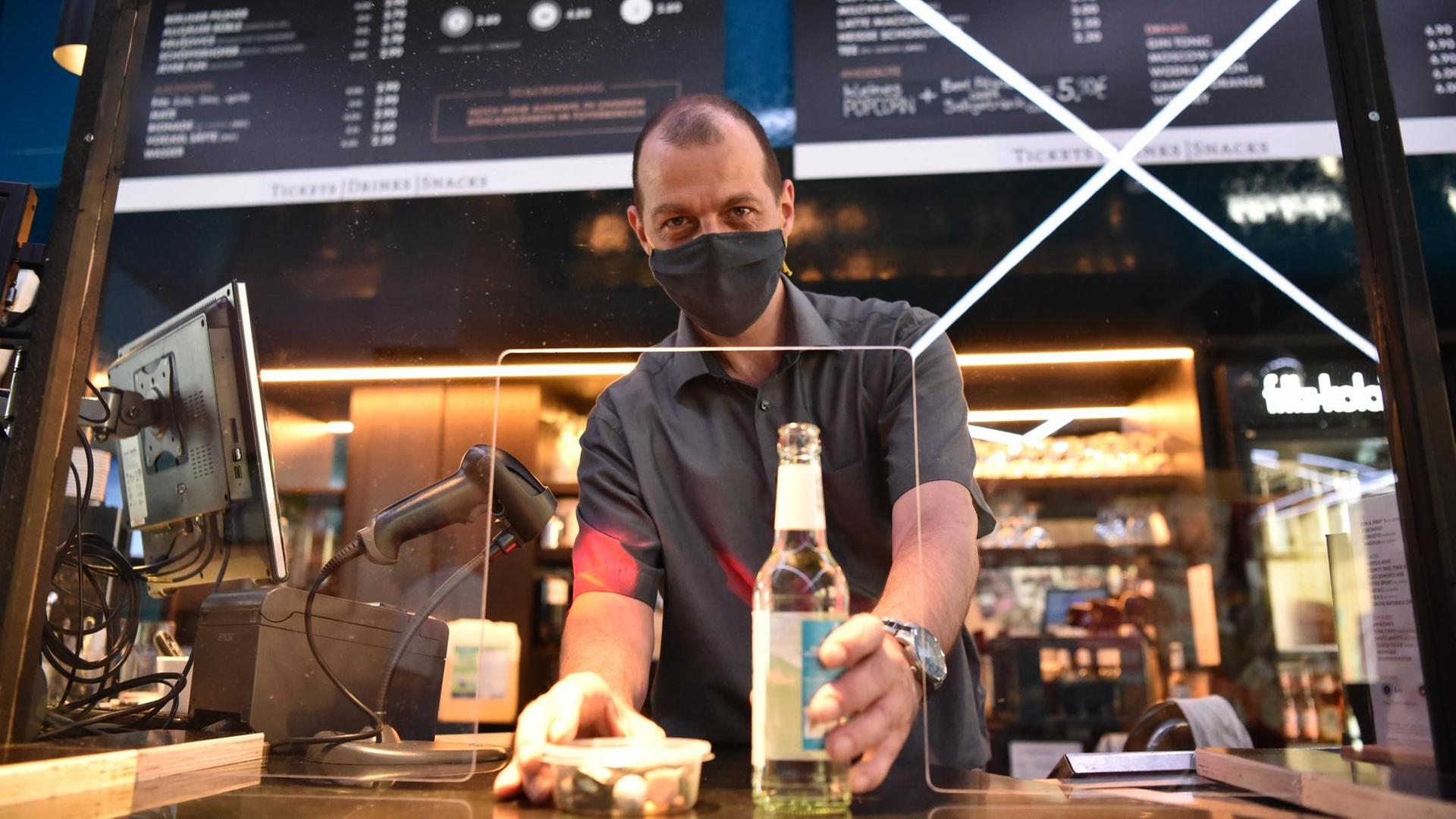 Ronald Graeber, Theaterleiter des Kinos Delphi Lux in Berlin-Charlottenburg, reicht Snacks und eine Flasche Wasser durch eine Plexiglasscheibe im Wartebereich des Gebäudes. Ronald Graeber, Theaterleiter des Kinos Delphi Lux in Berlin-Charlottenburg, reicht Snacks und eine Flasche Wasser durch eine Plexiglasscheibe im Wartebereich des Gebäudes.