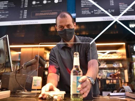 Ronald Graeber, Theaterleiter des Kinos Delphi Lux in Berlin-Charlottenburg, reicht Snacks und eine Flasche Wasser durch eine Plexiglasscheibe im Wartebereich des Gebäudes.