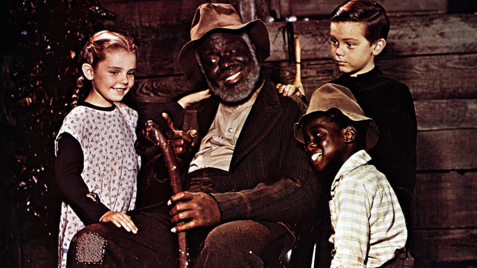 James Baskett als Onkel Remus sitz in einem Stuhl, umkreist von drei Kindern; Luana Patten als Ginny Favers, Bobby Driscoll als Johnny und Glenn Leedy als Toby.