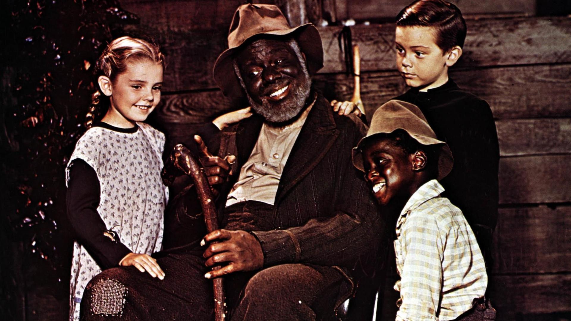 James Baskett als Onkel Remus sitz in einem Stuhl, umkreist von drei Kindern; Luana Patten als Ginny Favers, Bobby Driscoll als Johnny und Glenn Leedy als Toby. James Baskett als Onkel Remus sitz in einem Stuhl, umkreist von drei Kindern; Luana Patten als Ginny Favers, Bobby Driscoll als Johnny und Glenn Leedy als Toby.
