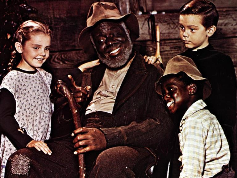 James Baskett als Onkel Remus sitz in einem Stuhl, umkreist von drei Kindern; Luana Patten als Ginny Favers, Bobby Driscoll als Johnny und Glenn Leedy als Toby.