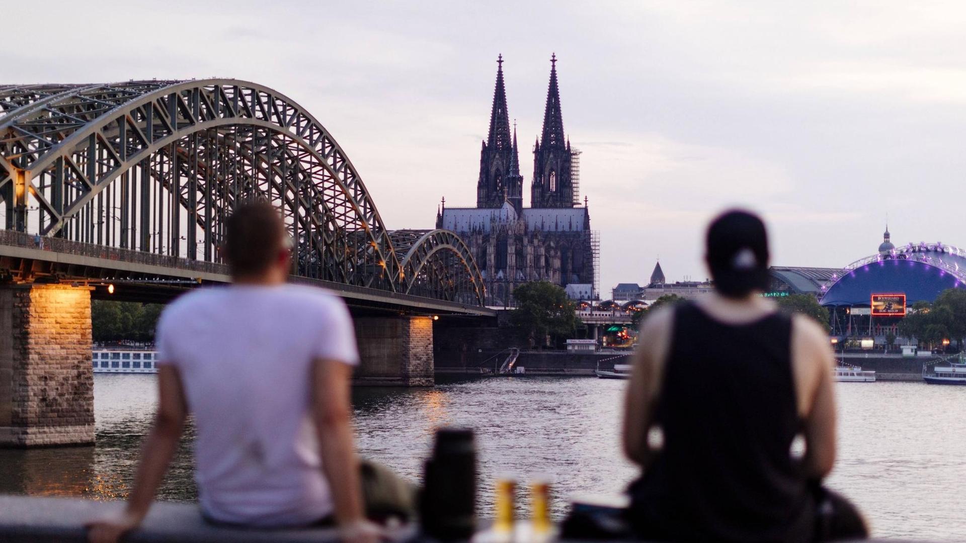 Kölner Skyline mit Kölner Dom, im Vordergrund trinken zwei Menschen Bier. Kölner Skyline mit Kölner Dom, im Vordergrund trinken zwei Menschen Bier.