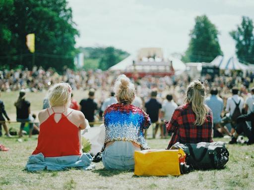 Drei junge Frauen sitzen gemeinsam auf einer Wiese und schauen auf das Festivalgelände.