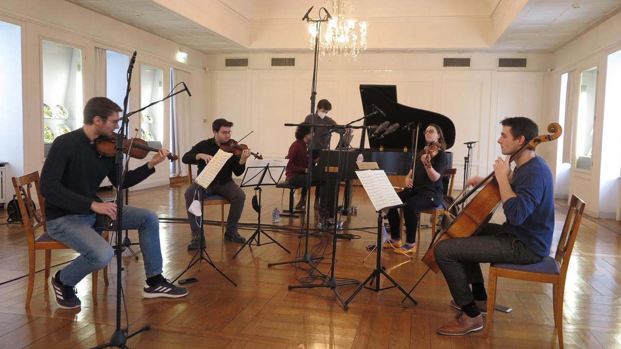 Fünf Musiker an ihren Streichinstrumenten und am Flügel zwischen Mikrofonen in einem Festsaal mit Parkettboden. Fünf Musiker an ihren Streichinstrumenten und am Flügel zwischen Mikrofonen in einem Festsaal mit Parkettboden.