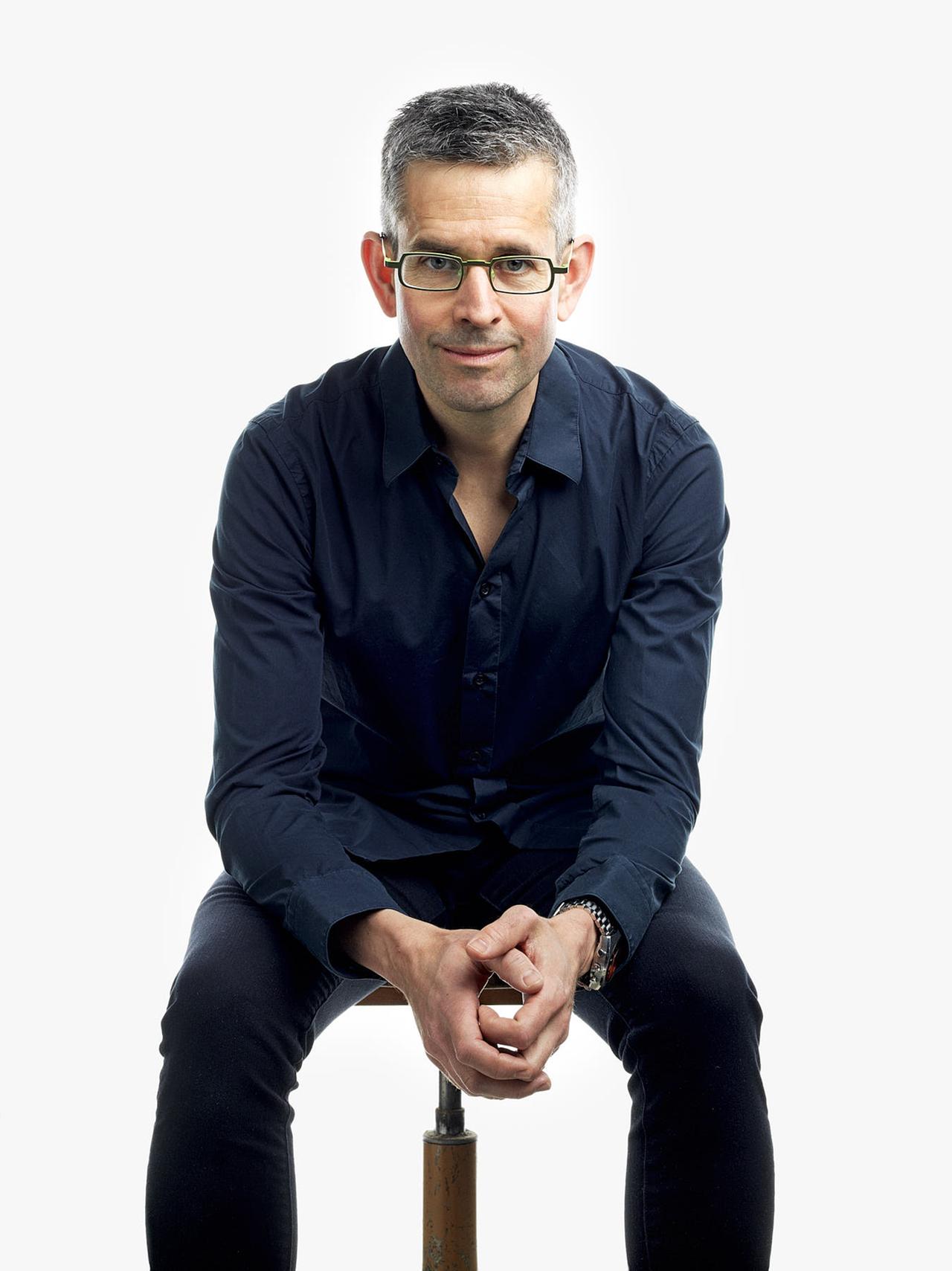 Ein Mann mit Brille sitzt auf einem Hocker Ein Mann mit Brille sitzt auf einem Hocker