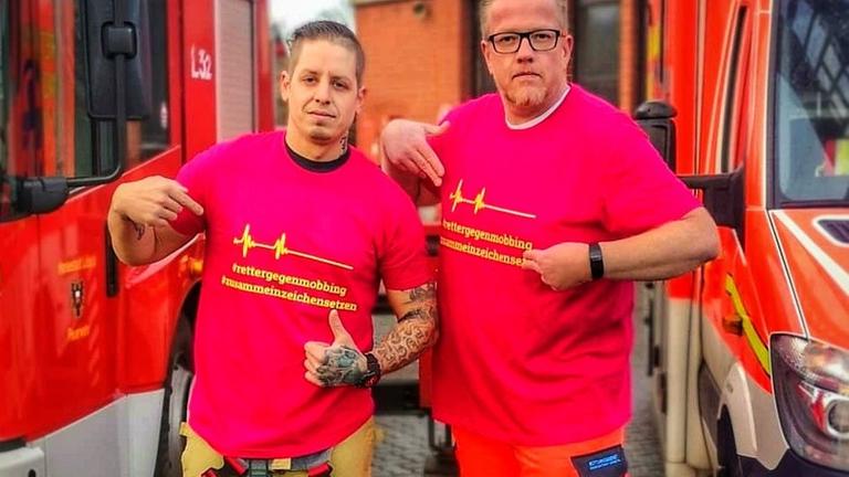 Zwei Feuerwehrmänner in Arbeitskleidung stehen zwischen zwei Feuerwehrautos. Zwei Feuerwehrmänner in Arbeitskleidung stehen zwischen zwei Feuerwehrautos.