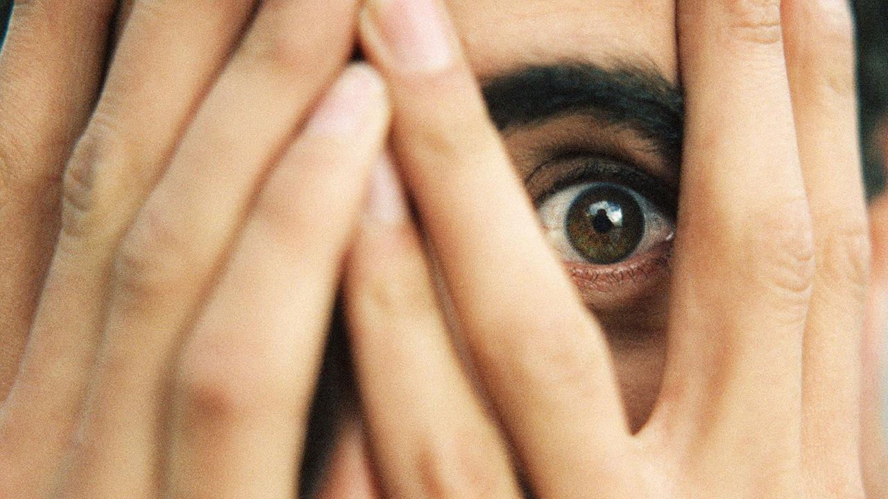 Ein Mann blickt ängstlich durch seine Hände, die er vor das Gesicht geschlagen hat. Ein Mann blickt ängstlich durch seine Hände, die er vor das Gesicht geschlagen hat.