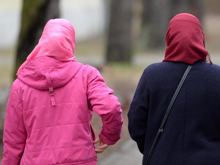 Man sieht zwei Frauen mit Kopftuch von hinten auf einer Allee.