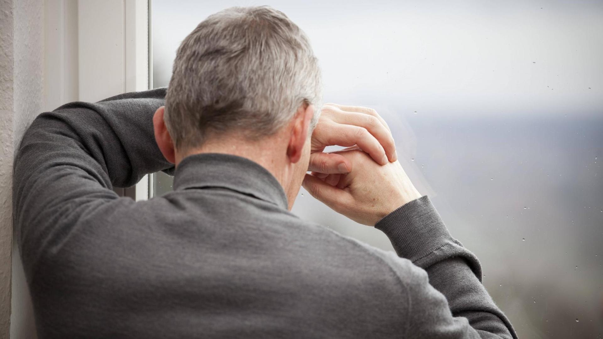 Ein Mann steht am Fenster und verbirgt aus Trauer sein Gesicht. Ein Mann steht am Fenster und verbirgt aus Trauer sein Gesicht.