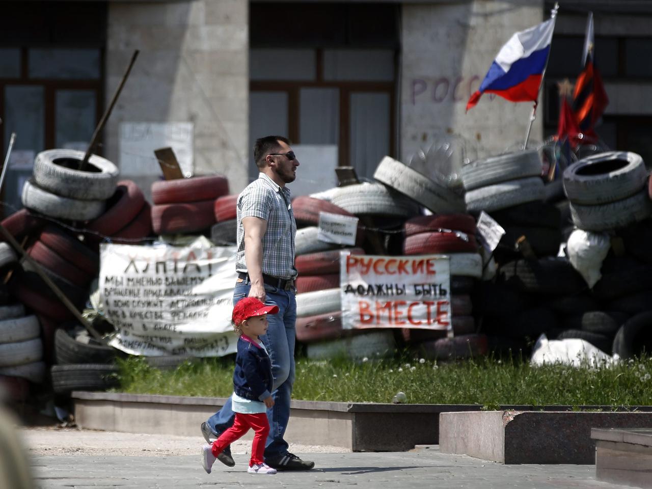 Ein Mann und ein Kind gehen an Barrikaden vor einem Verwaltungsgebäude in Donezk vorbei.