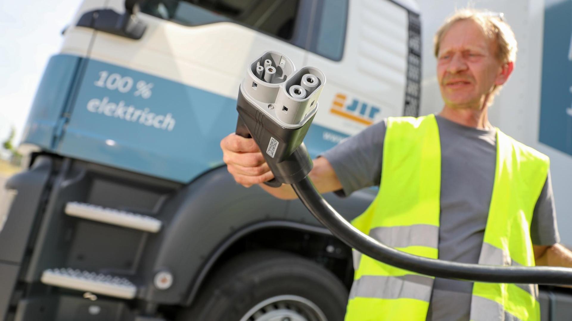 Der Mitarbeiter einer Spedition hält einen Ladestecker vor einem vollelektrischen 40-Tonnen-Elektro-Lkw des Forschungsprojekts eJIT Foto: Jan Woitas/dpa-Zentralbild/dpa | Verwendung weltweit Der Mitarbeiter einer Spedition hält einen Ladestecker vor einem vollelektrischen 40-Tonnen-Elektro-Lkw des Forschungsprojekts eJIT Foto: Jan Woitas/dpa-Zentralbild/dpa | Verwendung weltweit