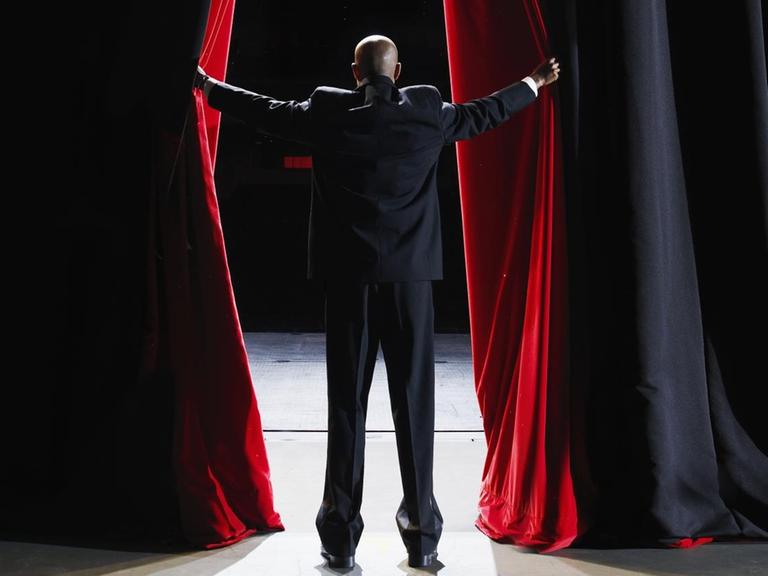 Ein Mann öffnet den roten Theatervorhang (Symbolbild).