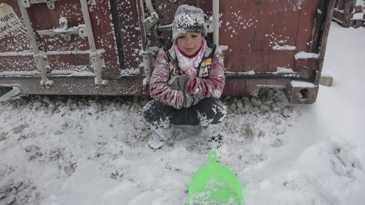 Ein Flüchtlingskind sitzt in einem griechischen Flüchtlingscamp im Schnee.
