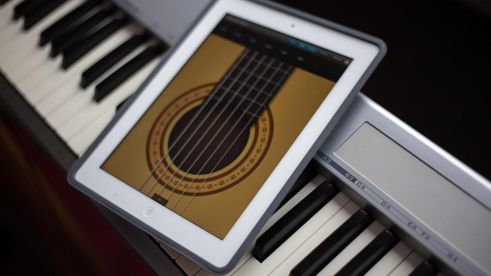 Auf einem Keyboard liegt ein Tablet Computer (iPad) mit einer Gitarren-App.
