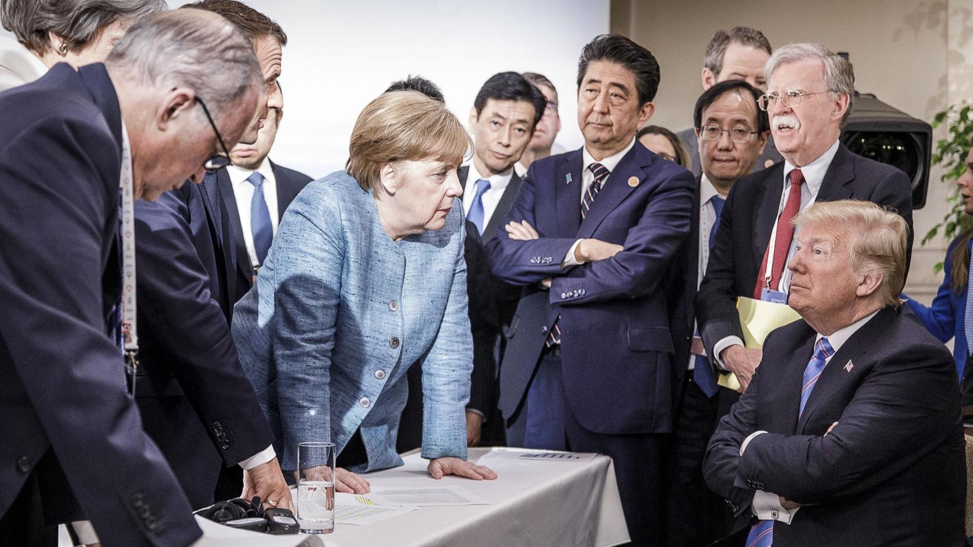 Angela Merkel stützt sich auf den Tisch, Donald Trump verschränkt die Arme beim G7-Gipfel in Kanada, 2018