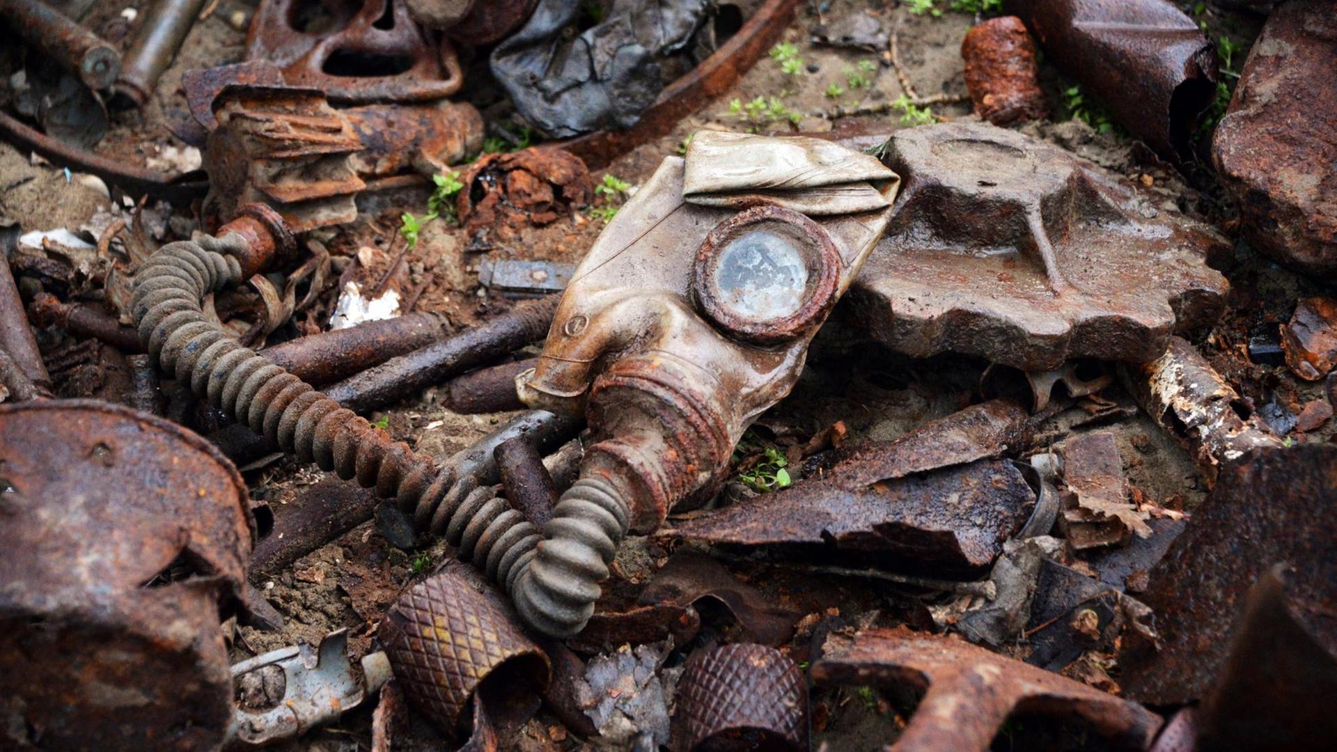 Überbleibsel einer Gasmaske und andere verrostete Metallteile aus dem Zweiten Weltkrieg liegen auf dem Boden.