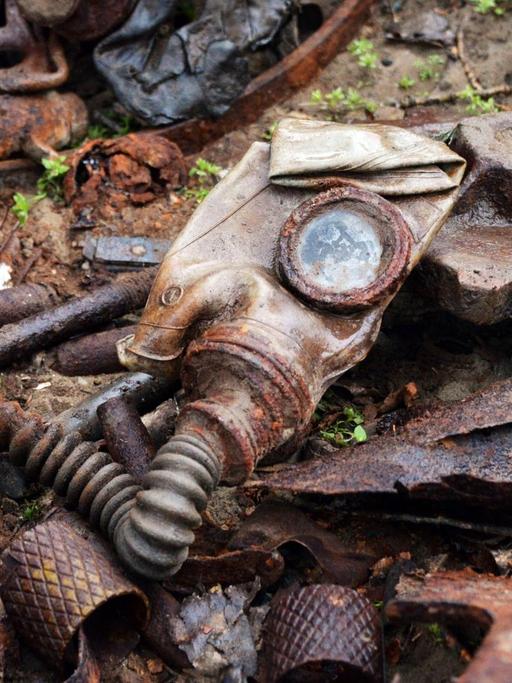 Überbleibsel einer Gasmaske und andere verrostete Metallteile aus dem Zweiten Weltkrieg liegen auf dem Boden.