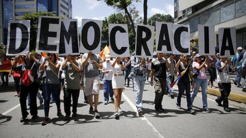 Regierungsgegner gehen wieder in Venezuelas Hauptstadt Caracas auf die Straße, sie halten die Buchstaben des Wortes "Demokratie" in die Luft.
